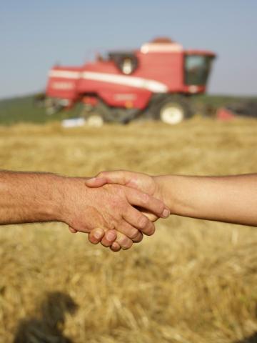 Shaking hands in a field with farm equipment in the background